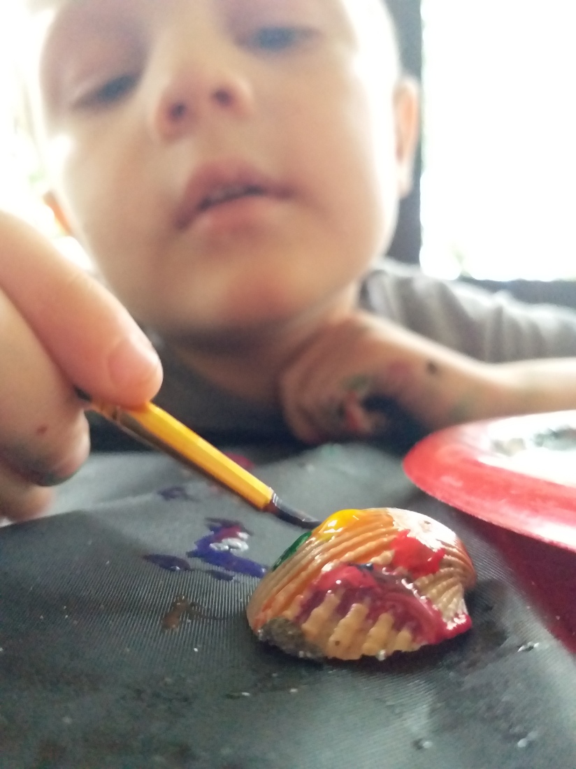 Boy painting a shell rainbow colors. As he practices emotional intelligence and self-awareness, he notes that his excitement is rainbow colored! 